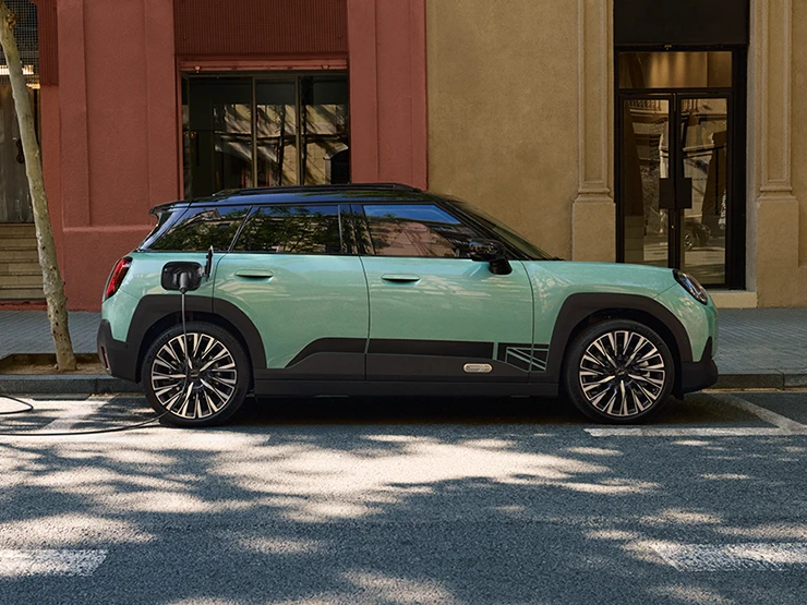 Vue latérale du MINI Aceman Electric Ocean Wave Green avec toit noir en charge en ville.