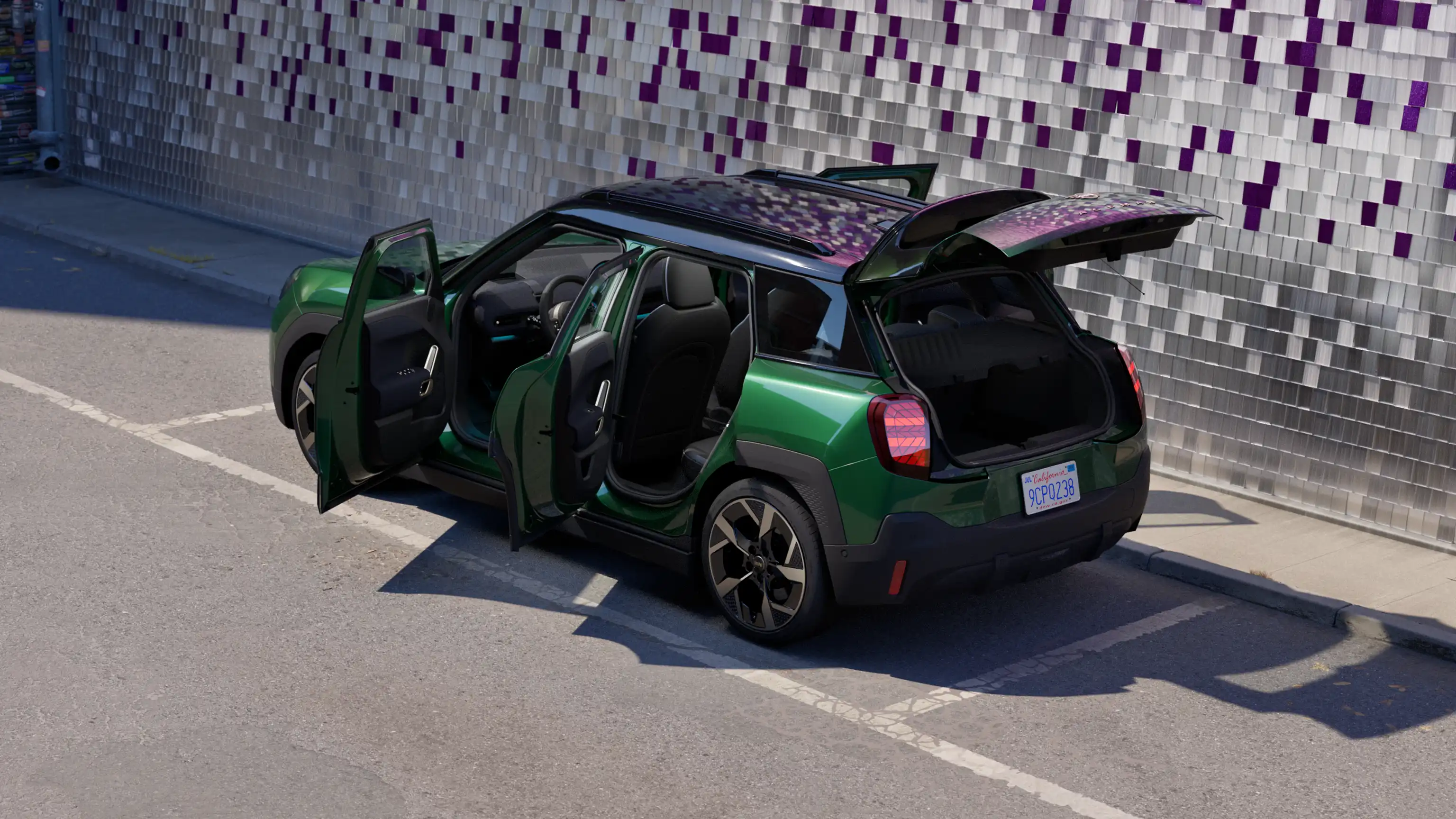 Vue latérale arrière d'un MINI Aceman 100 % électrique en British Racing Green stationné avec toutes les portes ouvertes et un mur coloré en arrière-plan