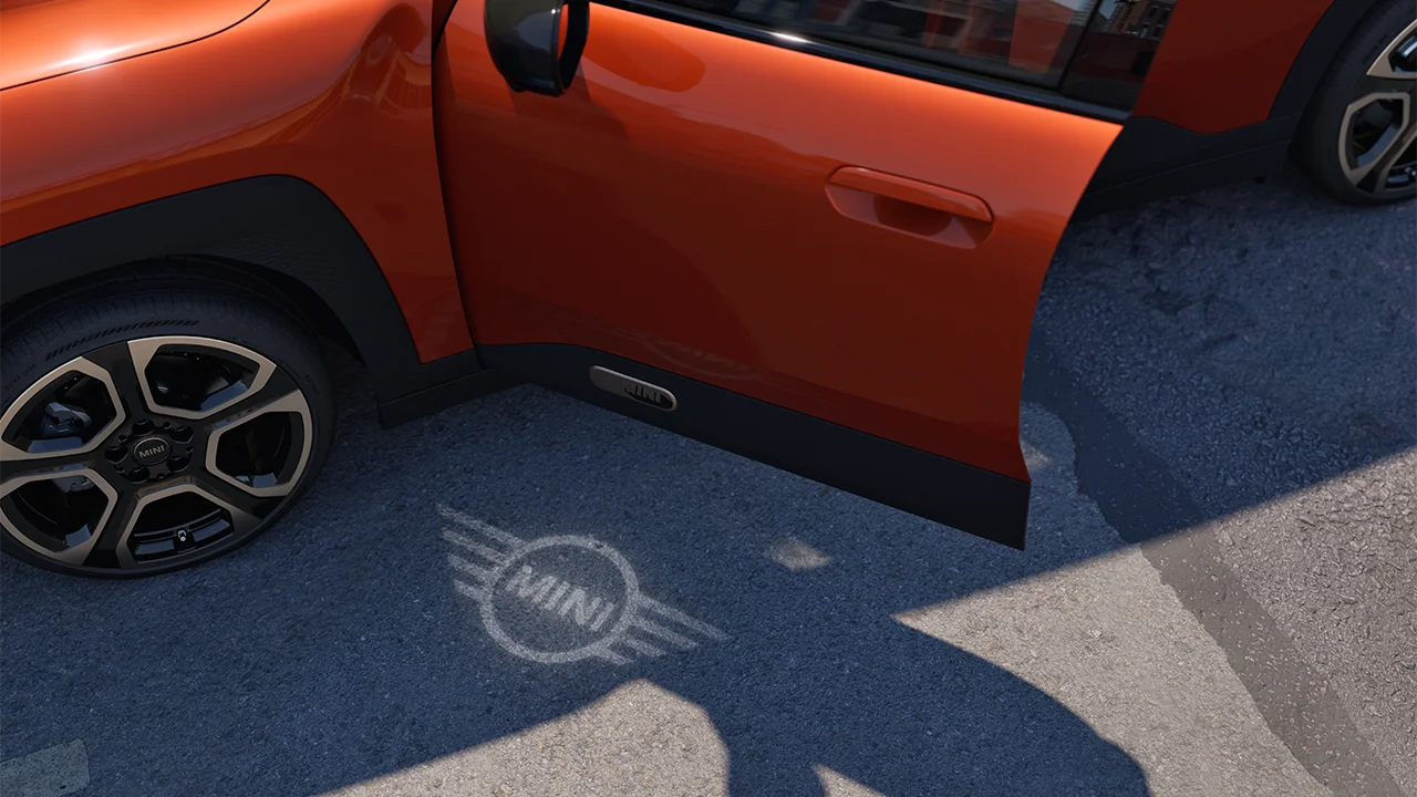 Vue extérieure du MINI Aceman 100 % électrique avec la porte ouverte et la lumière d’accueil du logo MINI projetée au sol