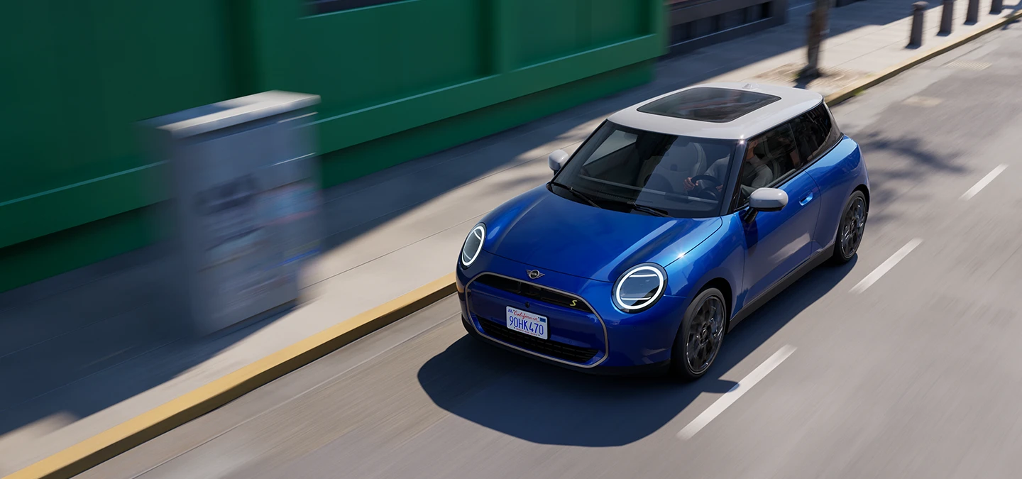 Vue du dessus de la MINI Cooper Electric Blazing Blue avec toit blanc roulant en ville. 