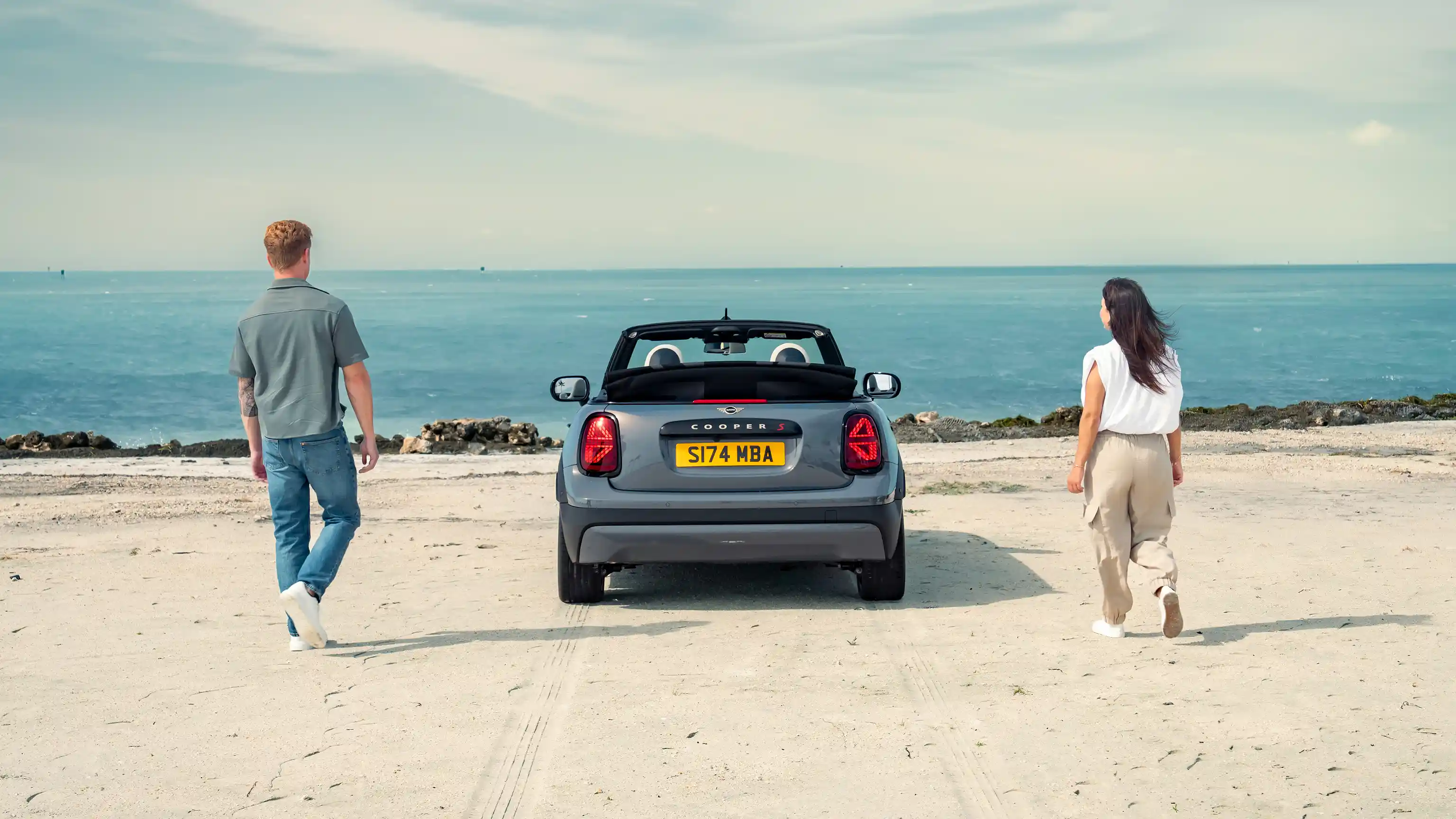 Vue arrière d'une MINI Cooper Cabrio garée à la plage avec deux personnes
