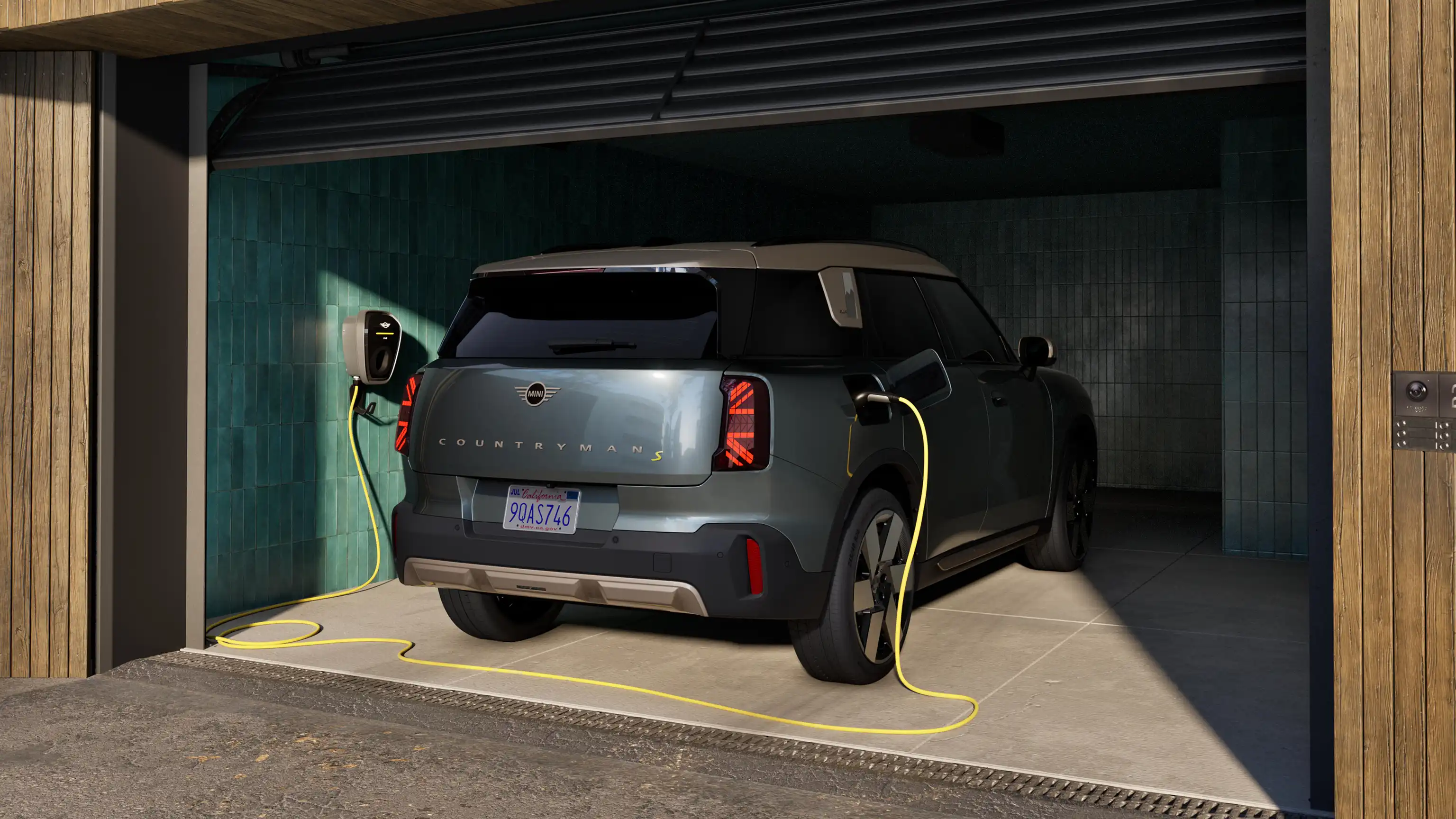 Vue arrière du MINI Countryman Electric en charge en Smokey Green, dans un garage ouvert, avec un câble de chargement connecté.