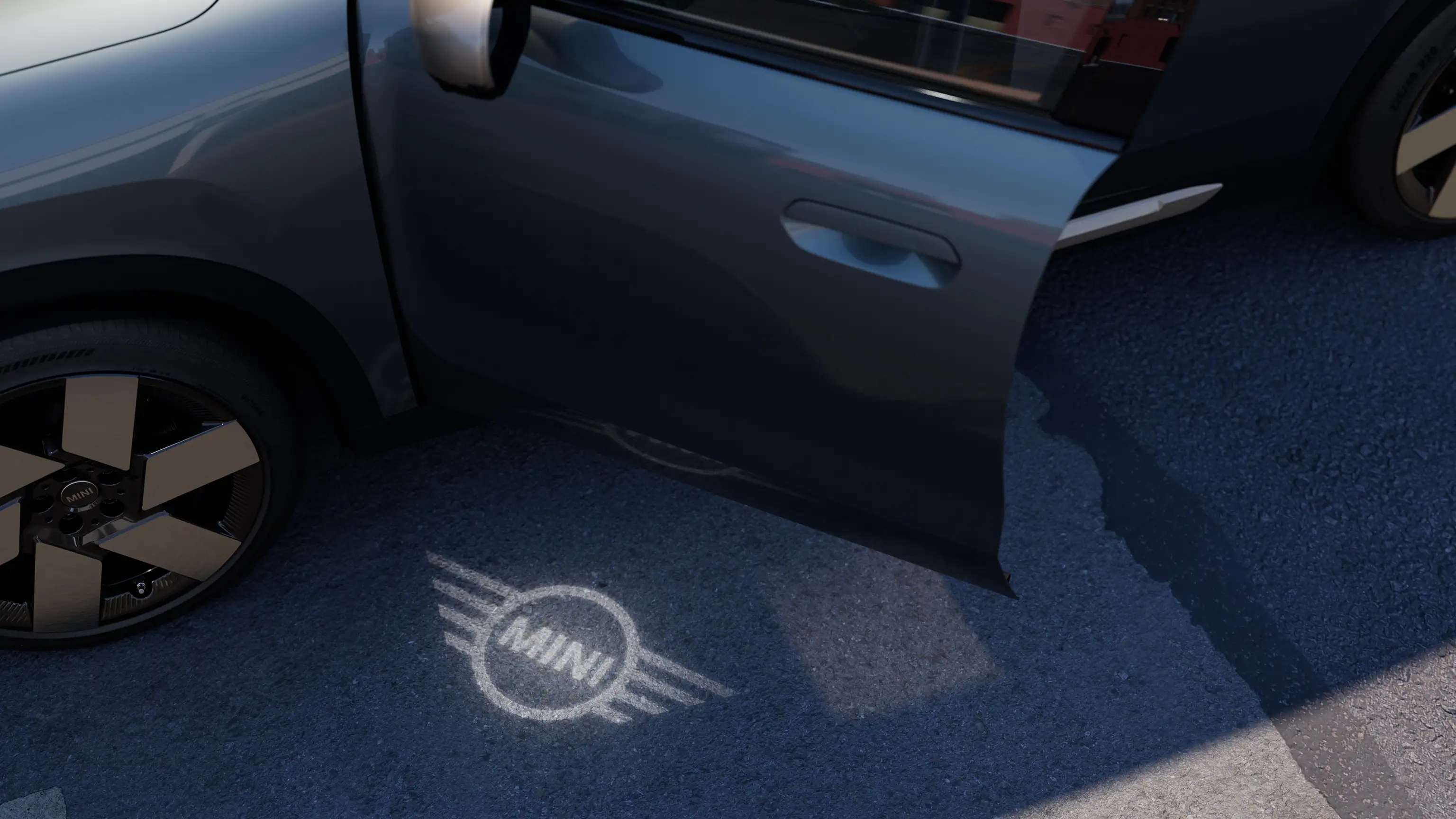 Vue extérieure du MINI Countryman Electric avec la porte ouverte et l'illumination d'accueil du logo MINI sur le sol.