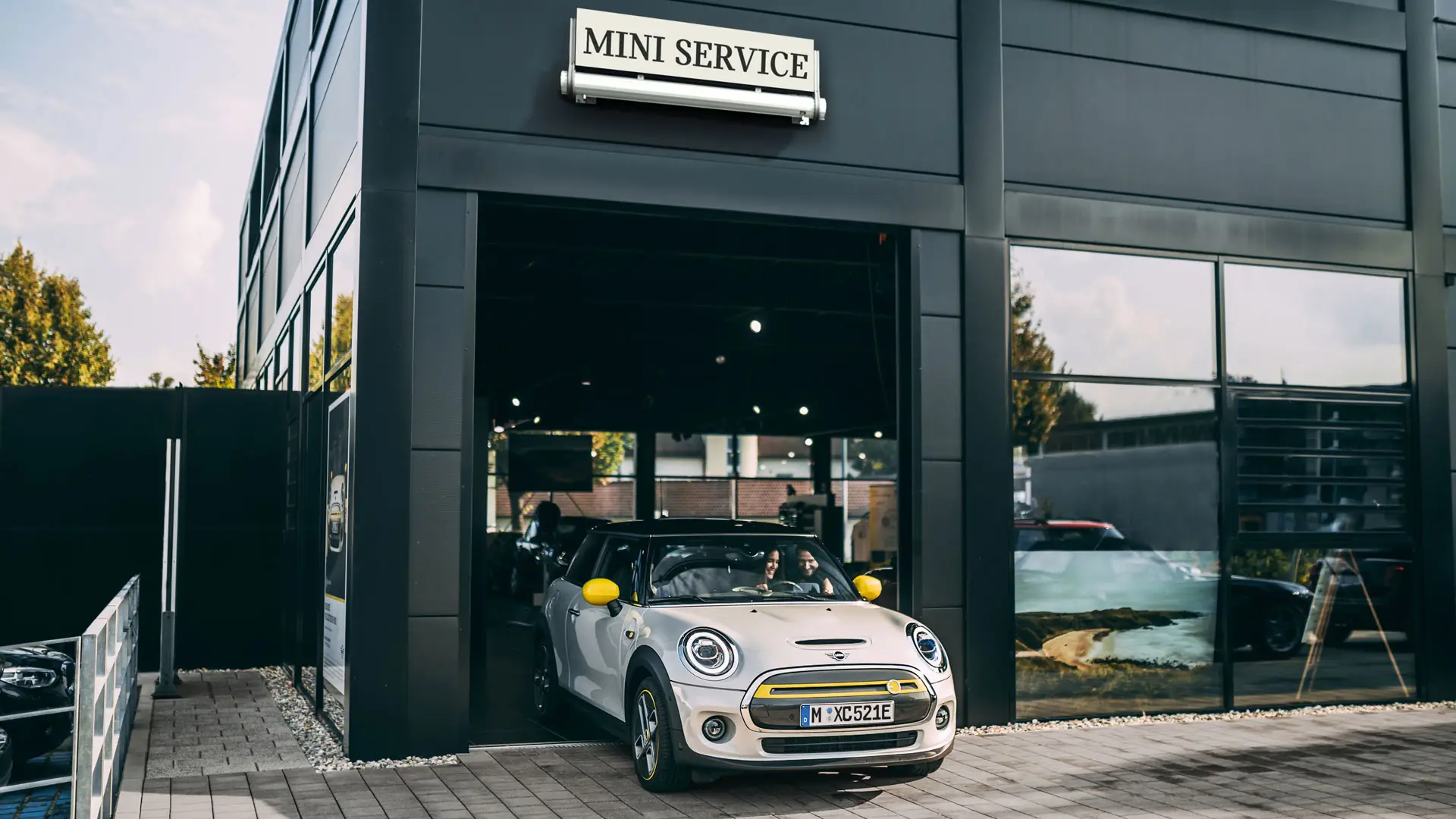 Dans les locaux d’un réparateur agréé MINI, une cliente conduit sa nouvelle MINI Electric sur le parvis