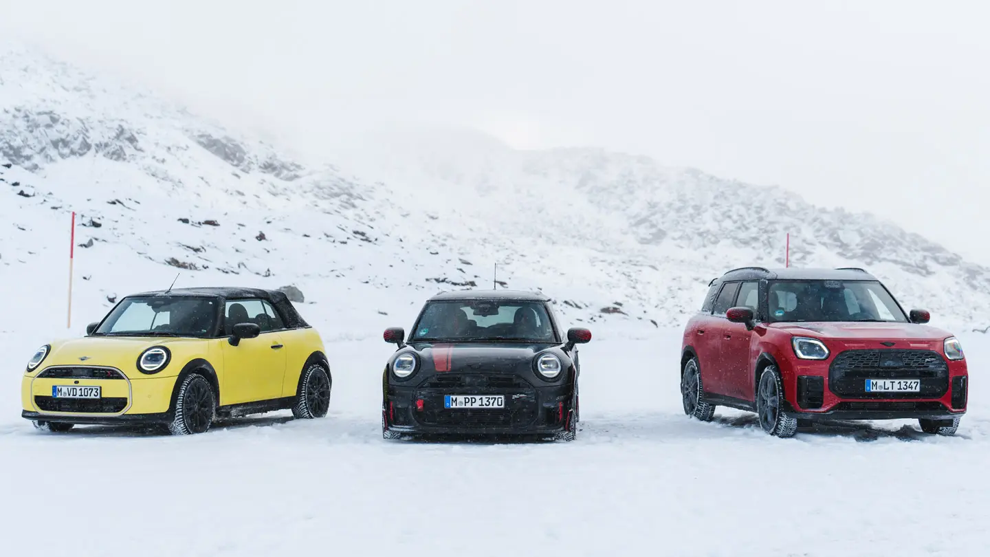 MINI Cooper Cabriolet en jaune Sunny Side, MINI John Cooper Works en Midnight Black II et MINI Countryman Cooper en Chili Red, à l’arrêt sur une route de montagne enneigée, vue de face.