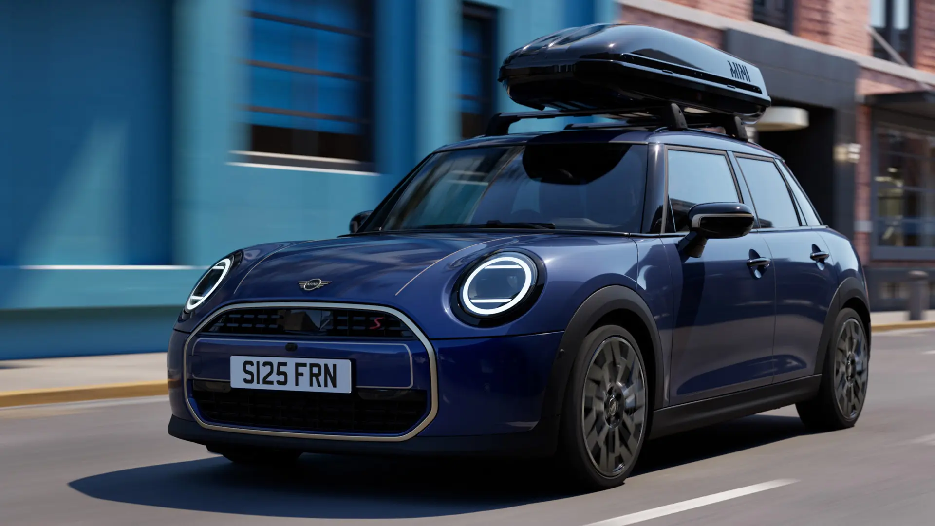 Vue trois quarts de face du MINI Aceman en Indigo Sunset Blue équipé de barres de toit MINI avec un coffre de toit MINI 320. 