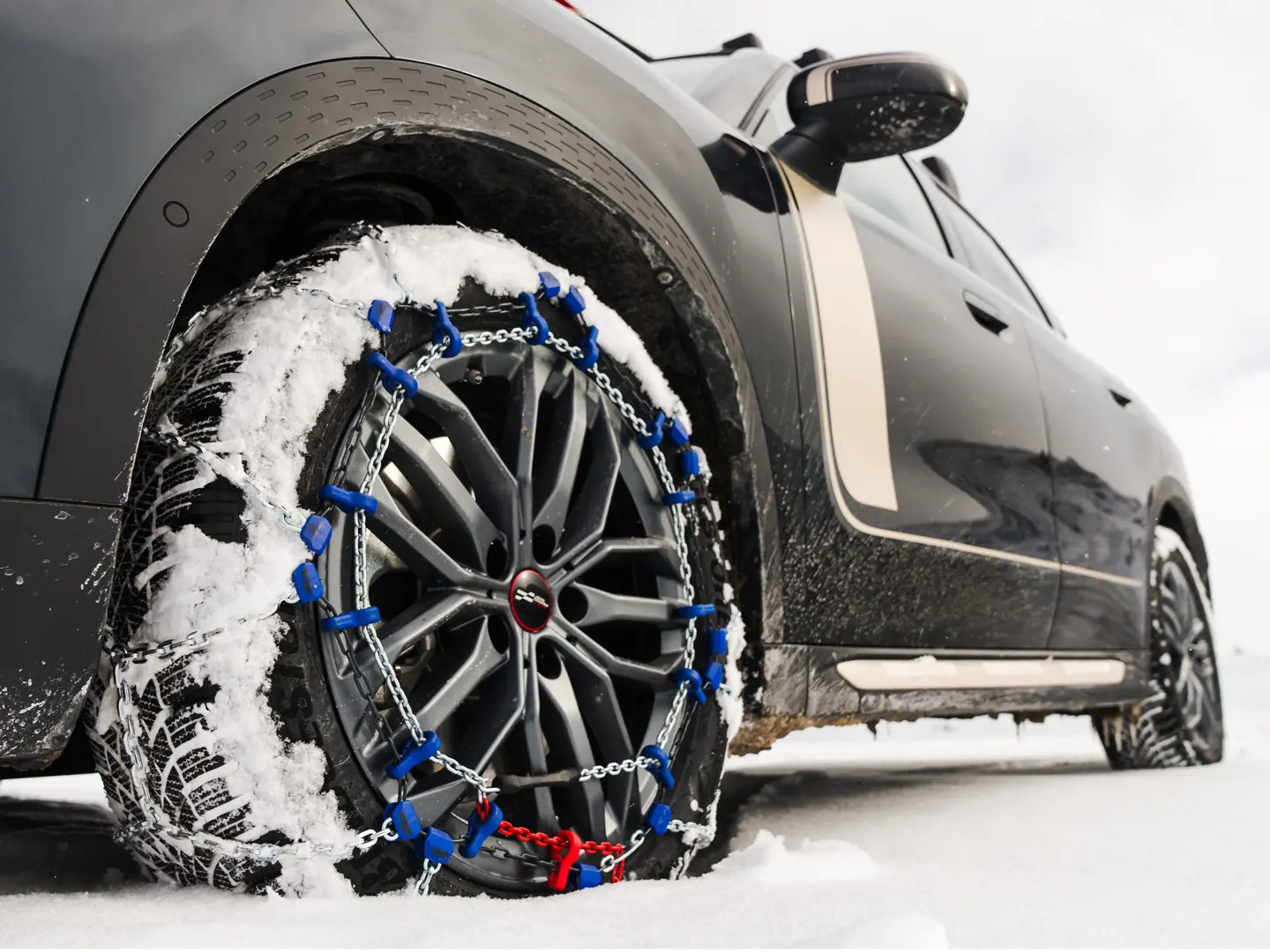 Gros plan d’une chaîne de pneus installée sur la roue d’un MINI Countryman pour une traction accrue lors de la conduite dans de fortes chutes de neige. 