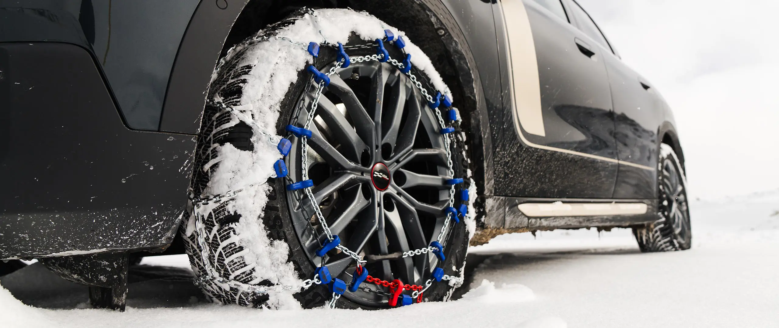 Gros plan d’une chaîne de pneus installée sur la roue d’un MINI Countryman pour une traction accrue lors de la conduite dans de fortes chutes de neige. 