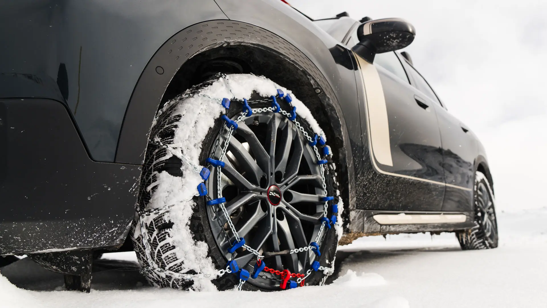 Gros plan d’une chaîne de pneus installée sur la roue d’un MINI Countryman pour une traction accrue lors de la conduite dans de fortes chutes de neige. 