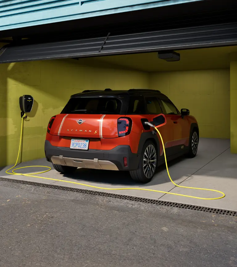 MINI Aceman S 100 % électrique stationné dans un garage, en cours de recharge avec la MINI Wallbox Plus, vue arrière.