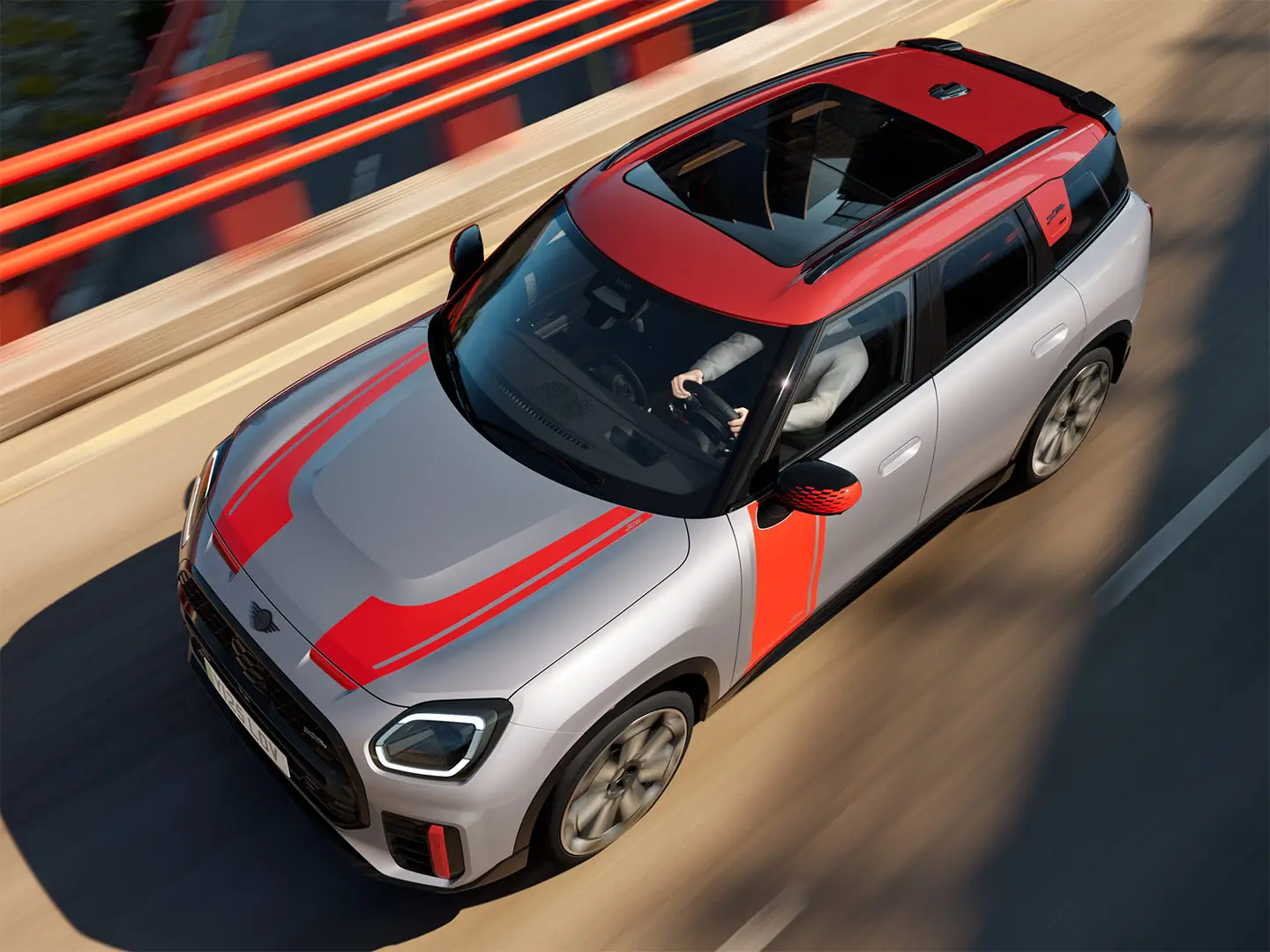 MINI Countryman John Cooper Works en Melting Silver avec coquille de rétroviseur, films latéraux et de capot, toit et ailettes Chili Red, roulant en ville, vue de face.